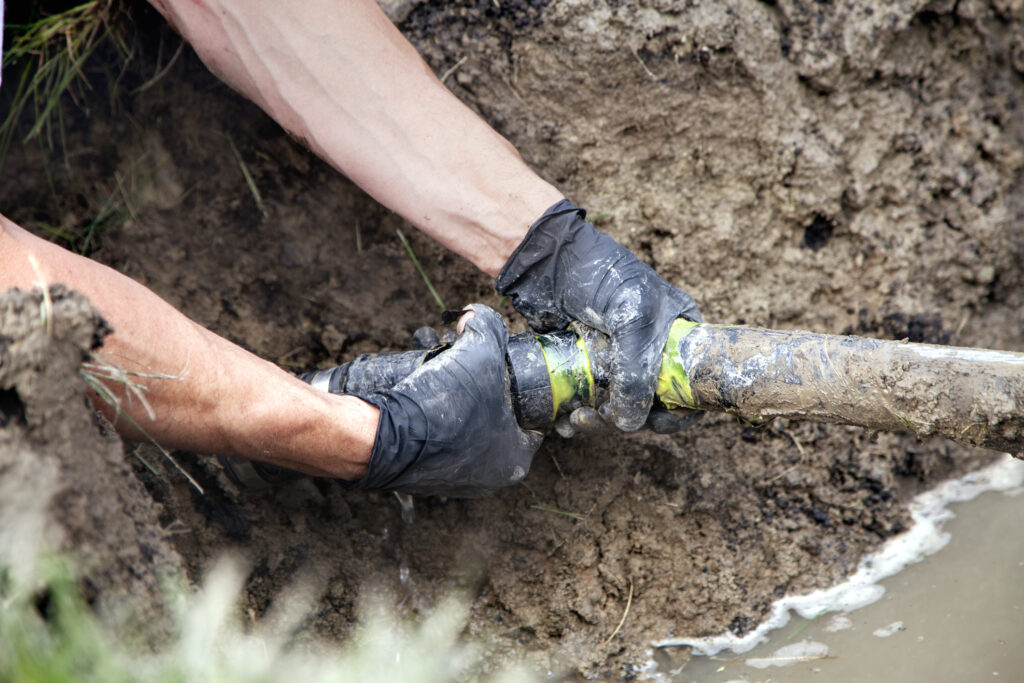 Plumber Repairing a Broken Pipe in a Septic Field